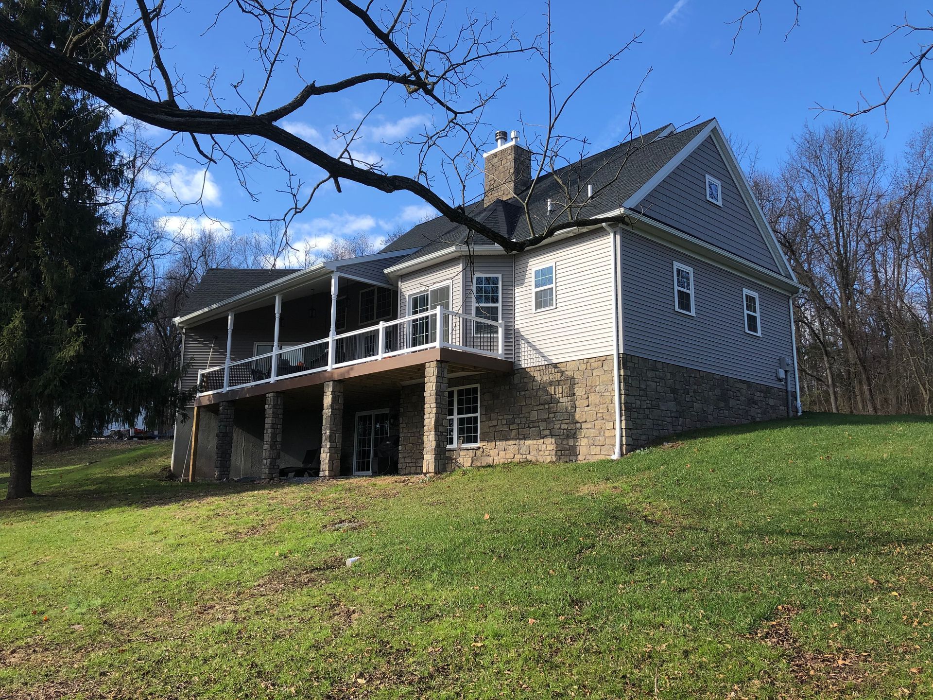 Gray two-story house with a porch on a grassy hill under a blue sky