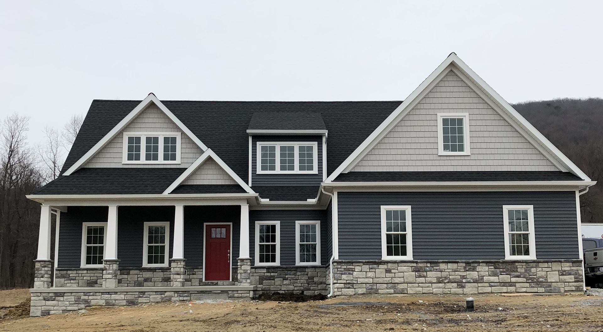 Gray farmhouse exterior with red front door and white trim under an overcast sky