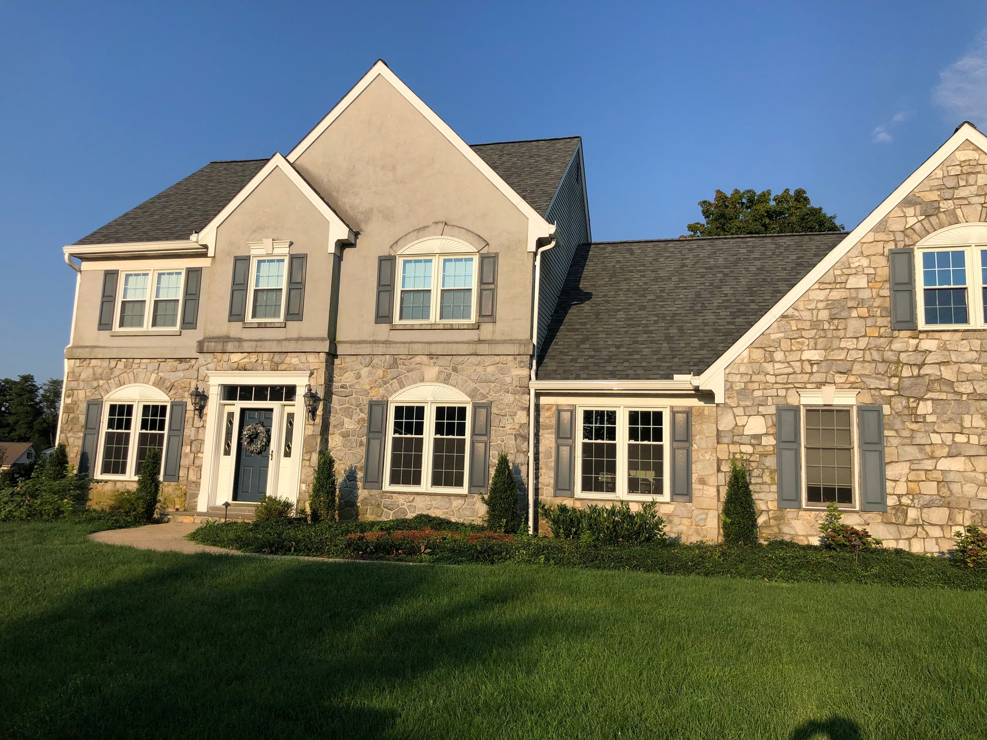 Large beige stone suburban house with dark gray roof and green lawn in front