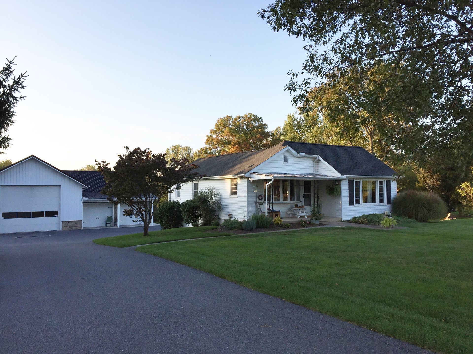White house with a detached garage, a wide driveway, and a green lawn at dusk