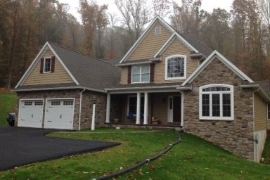 Large stone-and-siding suburban house with garage, front porch, and autumn trees in the background