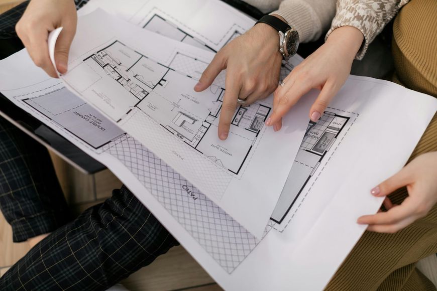 Hands reviewing a floor plan blueprint on a table with pencils and papers