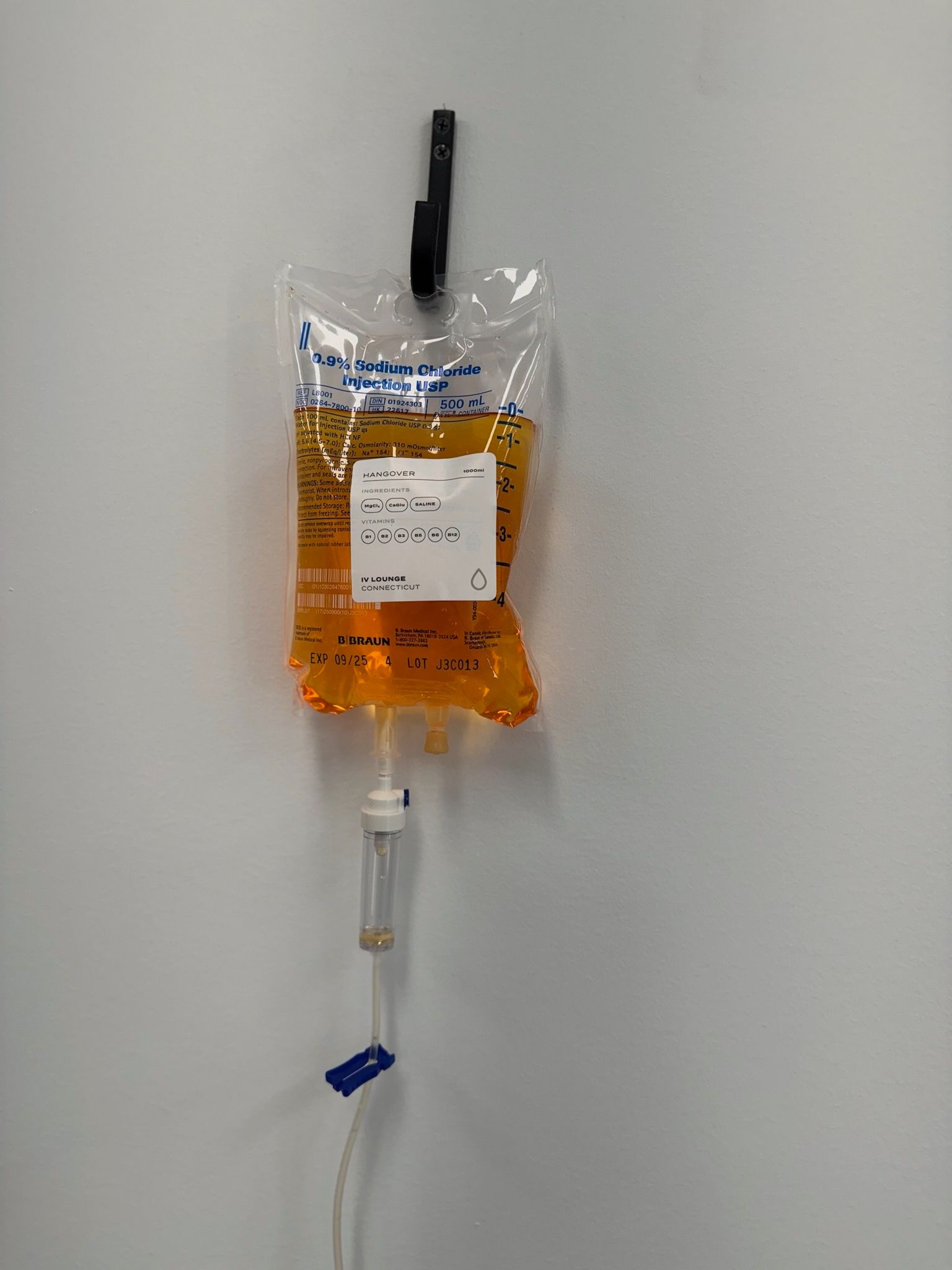 IV bag with orange liquid hanging on a hook on a white wall.