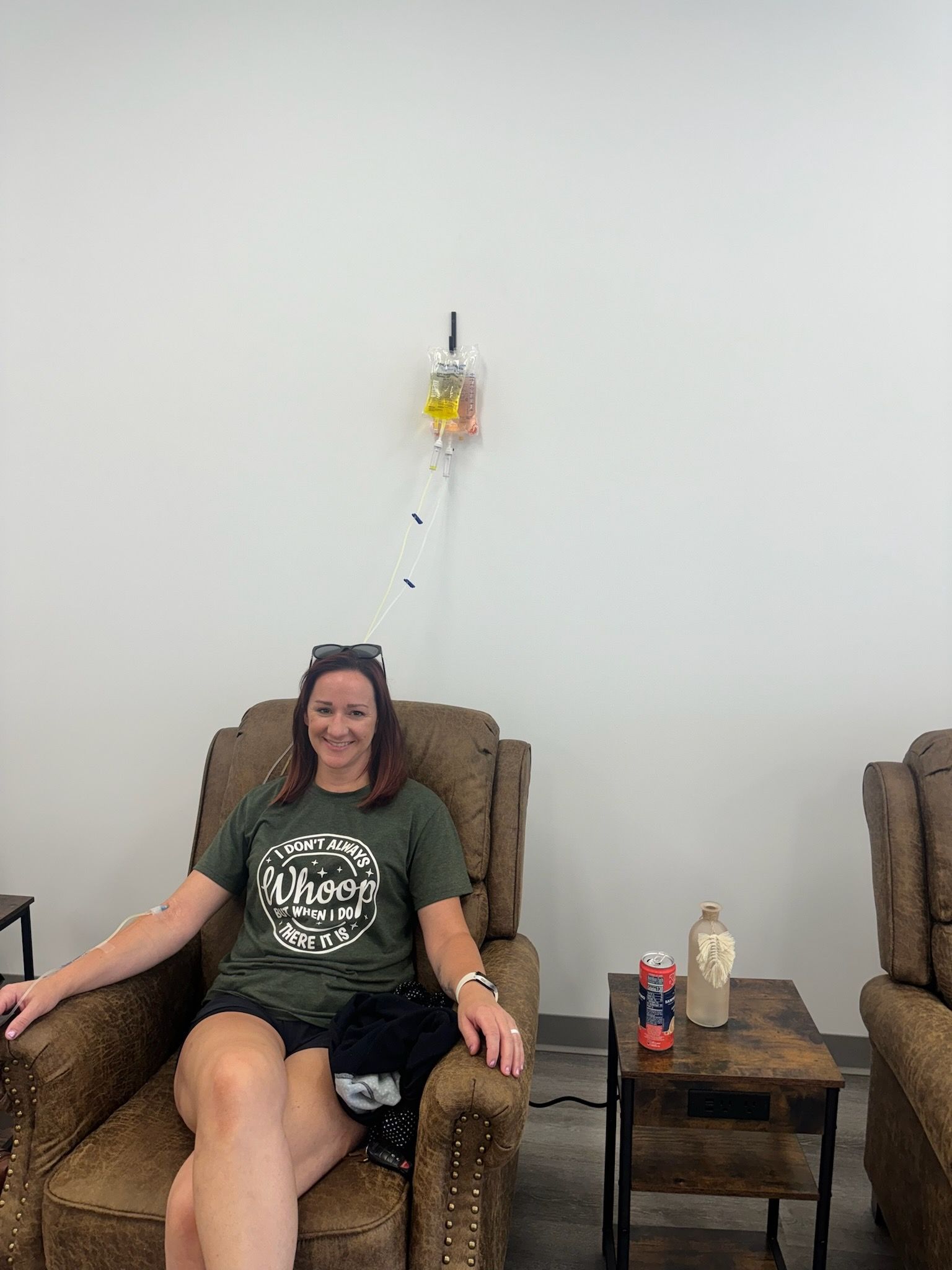 Woman in recliner with IV drip, smiling. Brown recliner, white wall, small table with a drink.