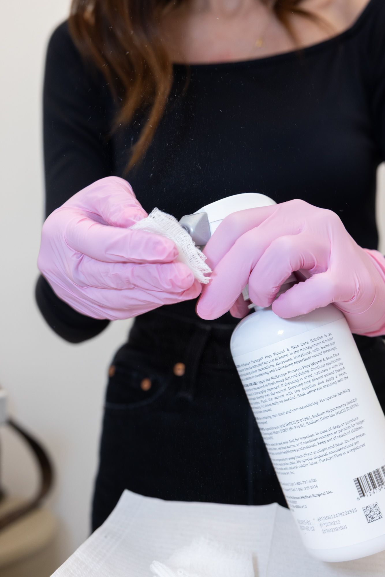 A doctor in pink gloves spritzes something from a bottle onto a white cloth.