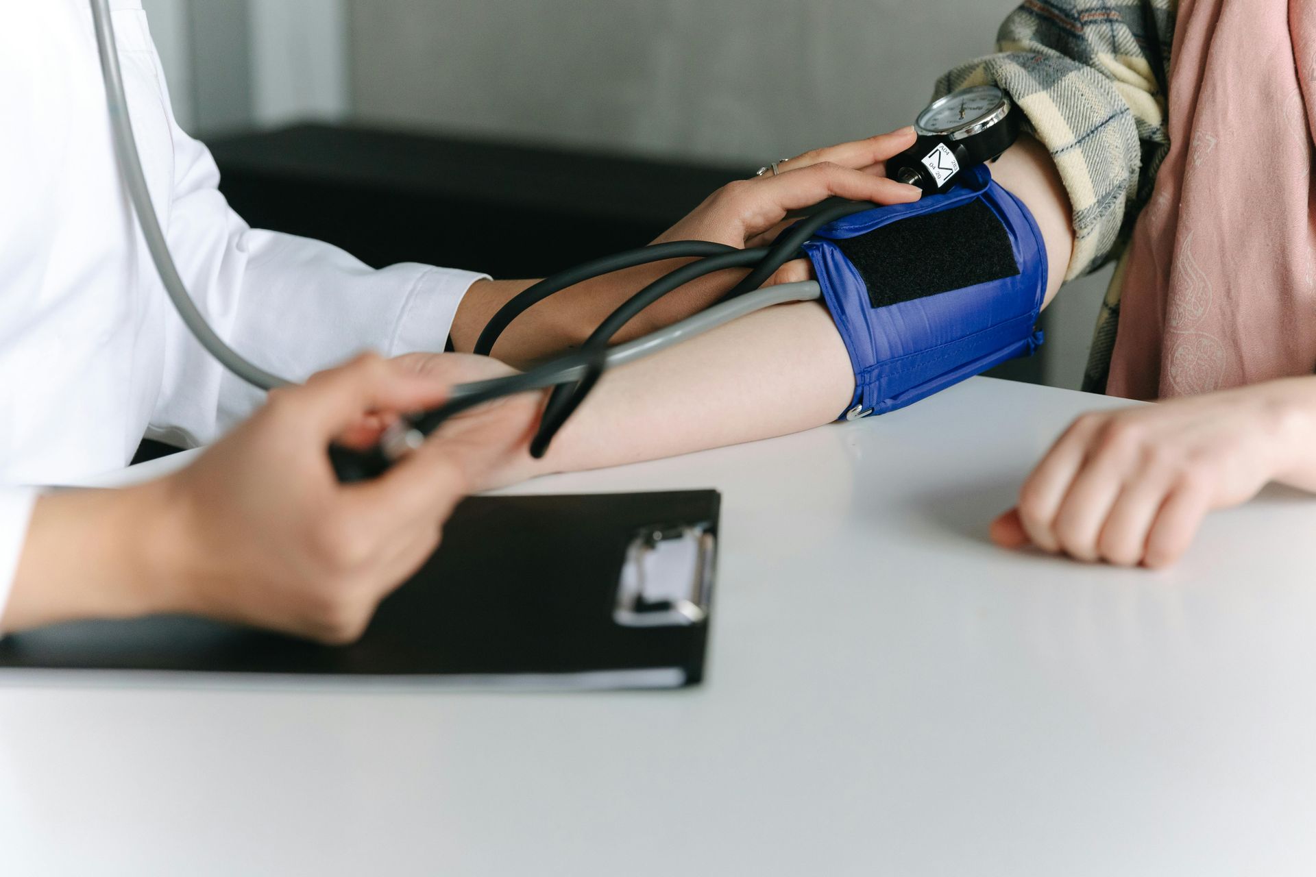Doctor taking patient's blood pressure with a blue cuff and stethoscope in a medical setting.