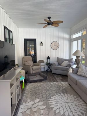 Woman making bed in a bright bedroom with a window, smiling while holding items.