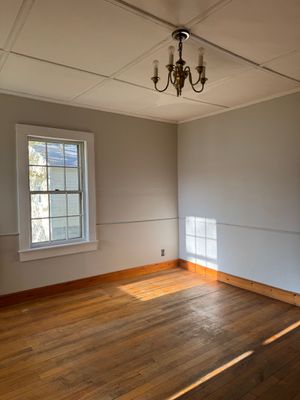 Two construction workers sweeping dusty interior space with large windows.