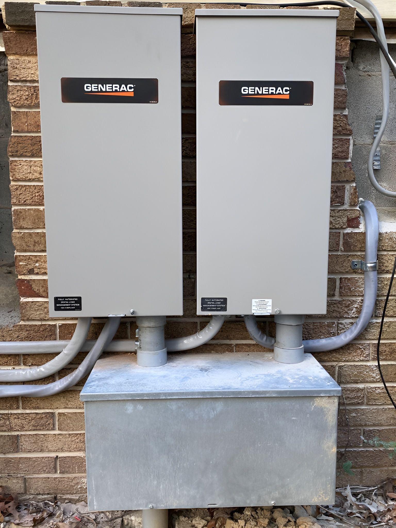 Two gray Generac electrical boxes mounted on a brick wall with conduit.