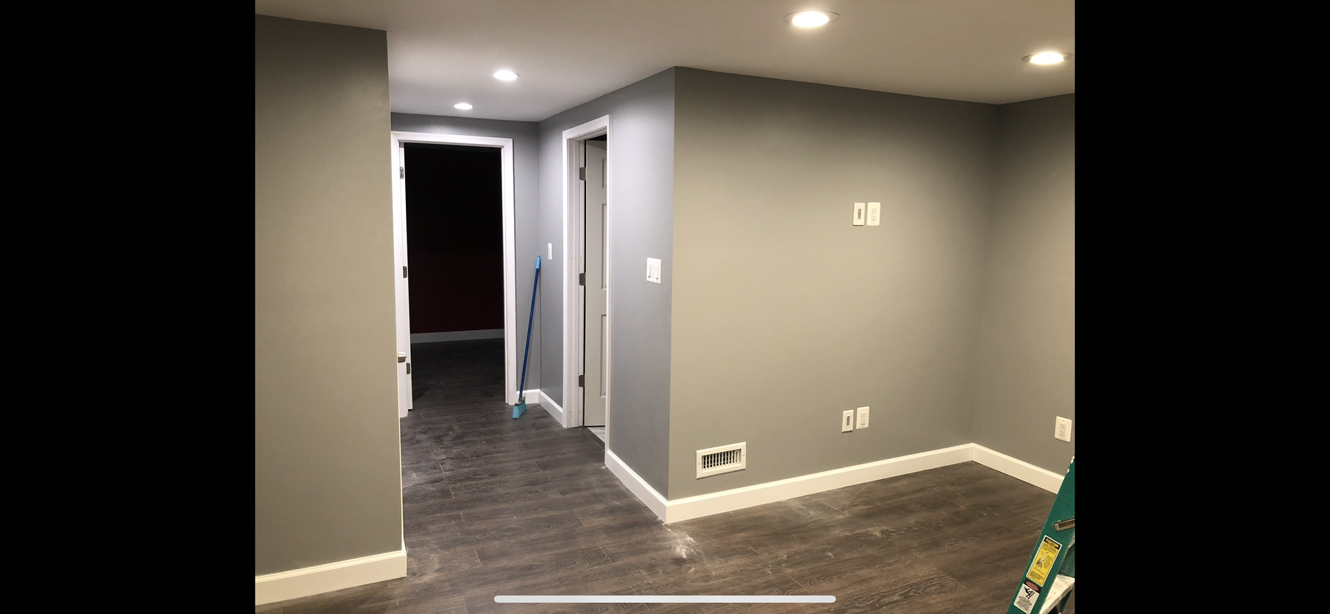 A room painted gray with white trim, doors, and recessed lighting. A dark hallway is visible.