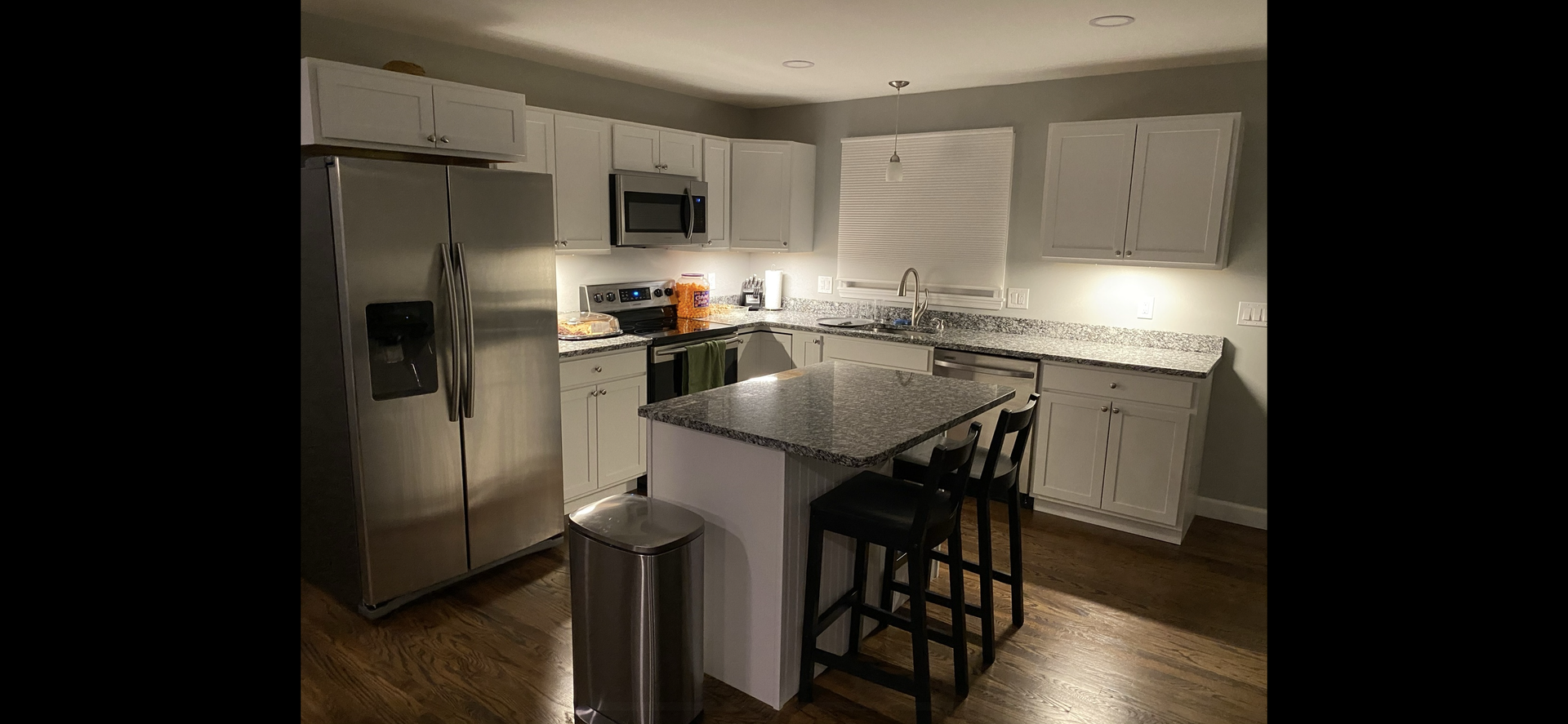 Kitchen with white cabinets, stainless steel appliances, and a dark-topped island with two stools.