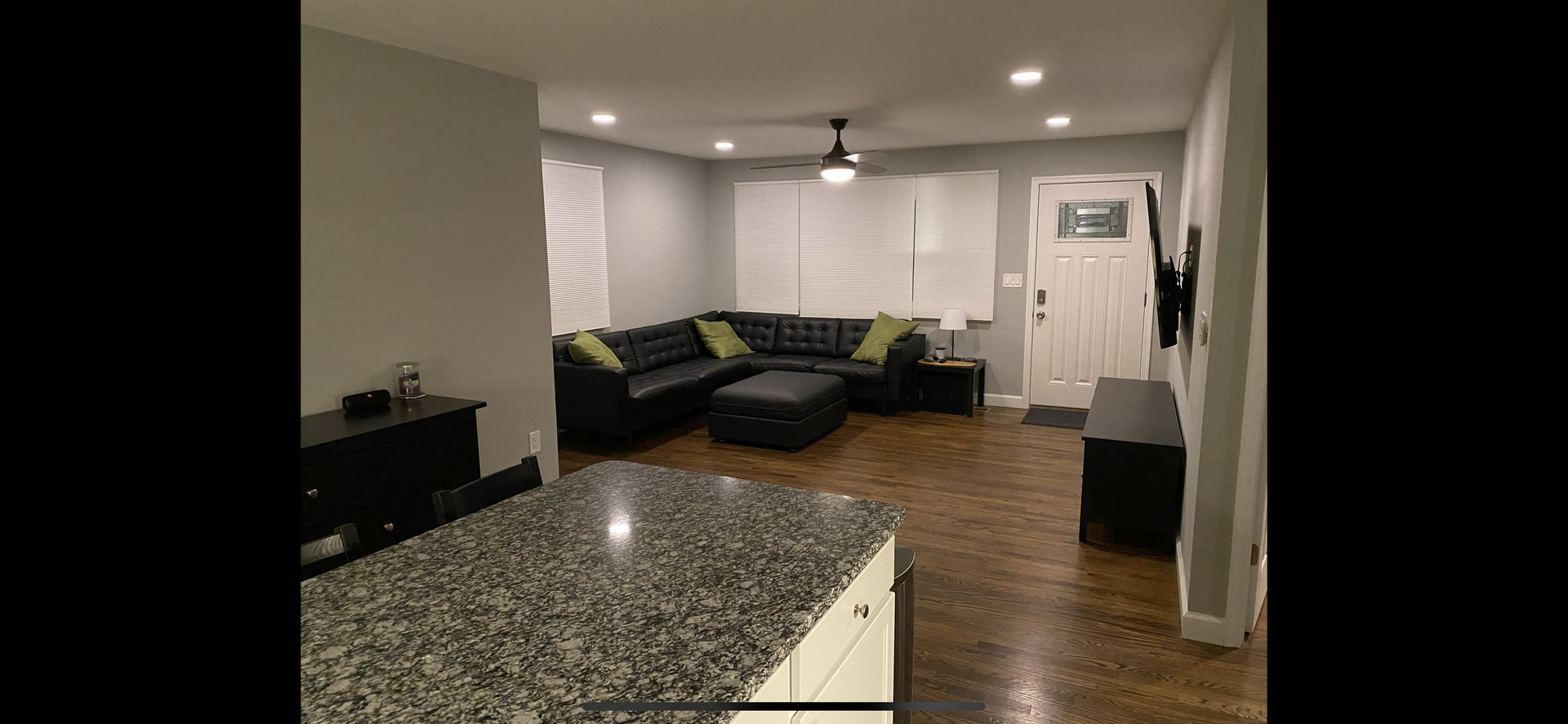 Living room with black sectional, wood floors, granite countertop, and gray walls.