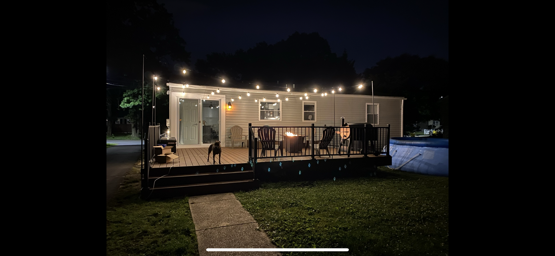 A lit deck at night with a small dog and lights strung across the roof.