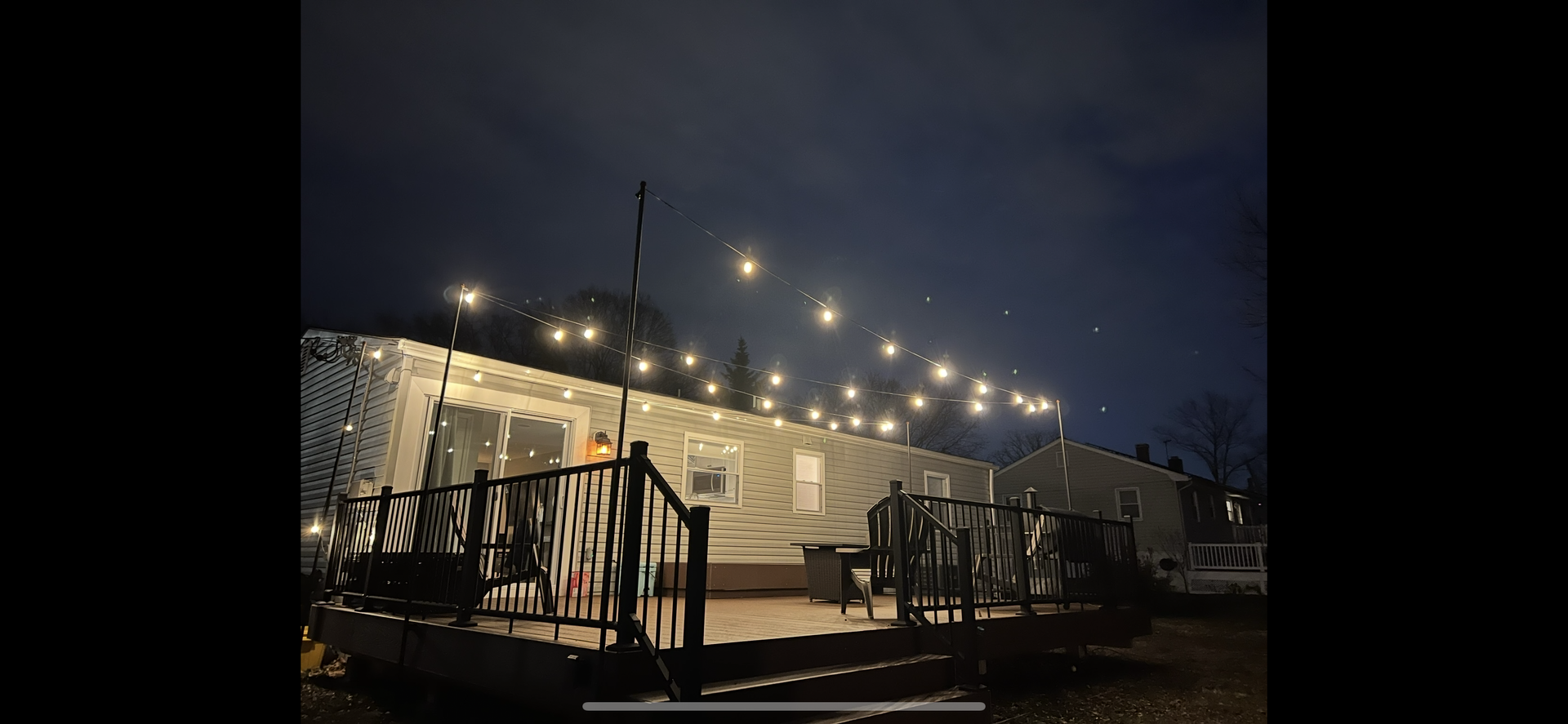 Night view of a deck with string lights and a house in the background. The sky is dark.