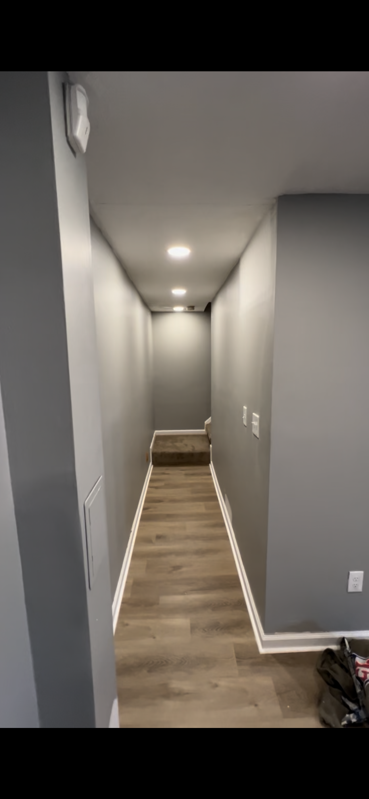 Narrow hallway with grey walls, recessed lights, and wood-look flooring leading to a small flight of steps.