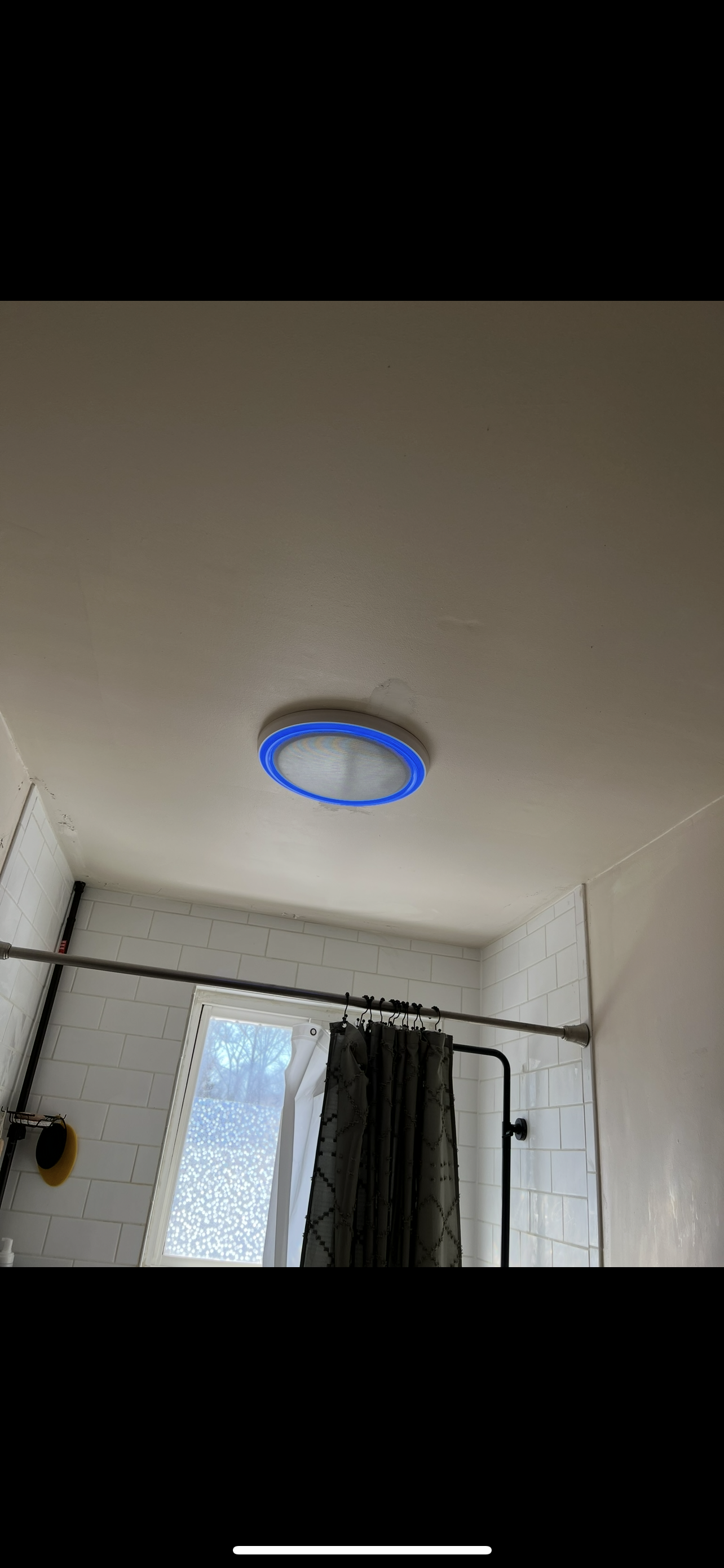 Bathroom ceiling light with a blue halo, above a shower curtain and window.