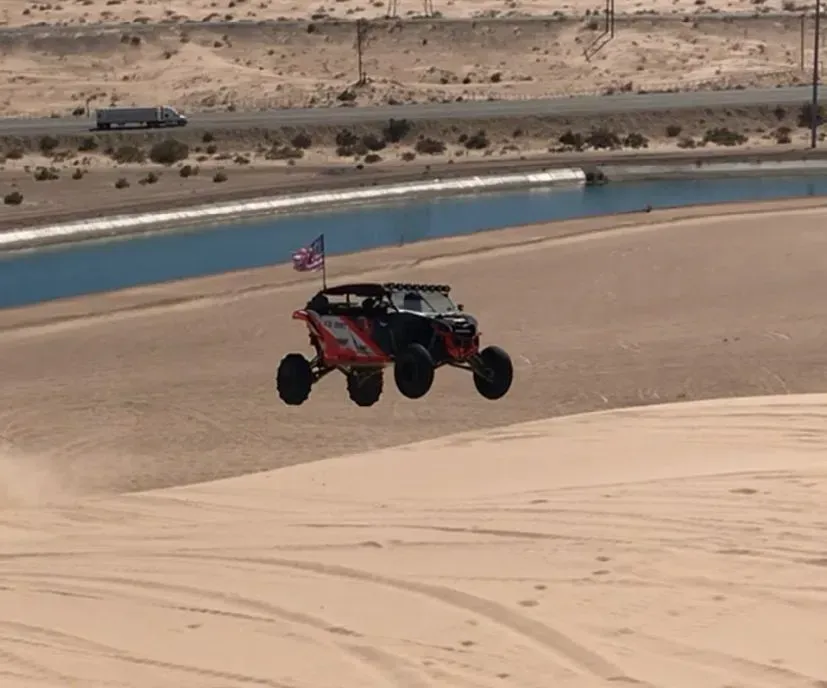 A red and white atv is flying over a sand dune.