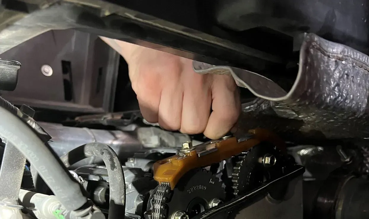 A person is working on a car engine with a wrench.