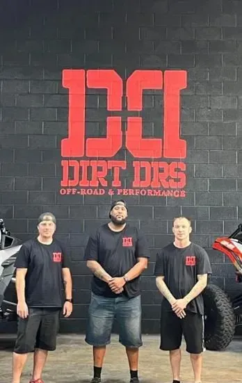 Three men are standing in front of a dirt drs sign.