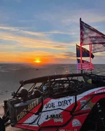 A can am maverick r3 is parked on the beach at sunset.