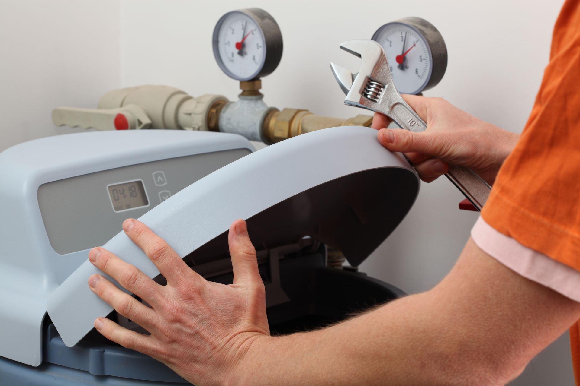 A man uses a wrench to adjust a water softener, a device designed to reduce mineral content in water for improved household water quality.