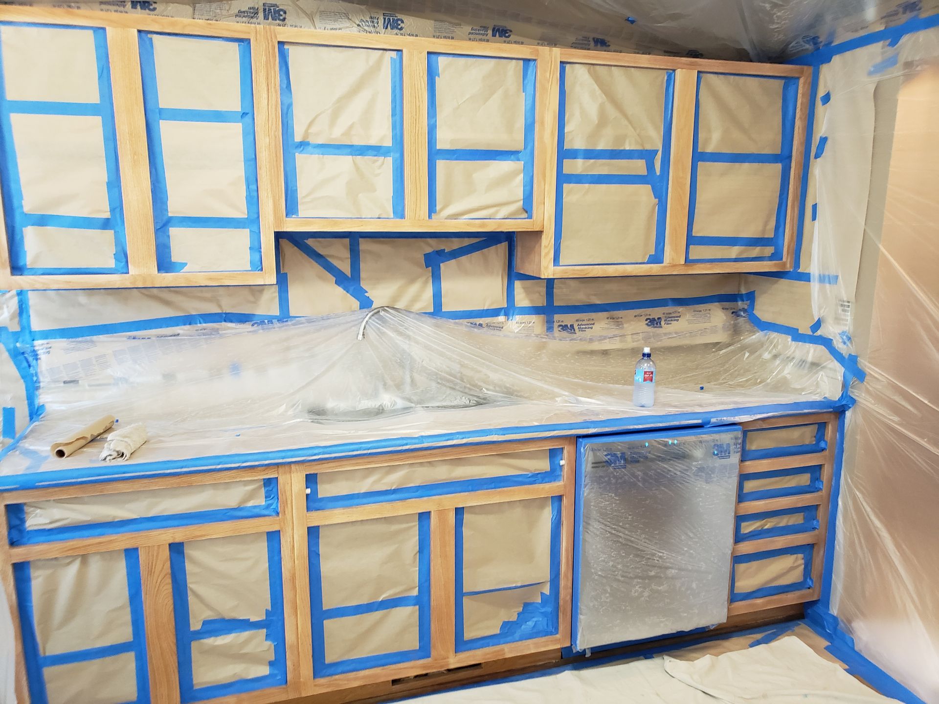 Kitchen prep phase for cabinet refinishing with frames masked off and protected using paper and plastic.