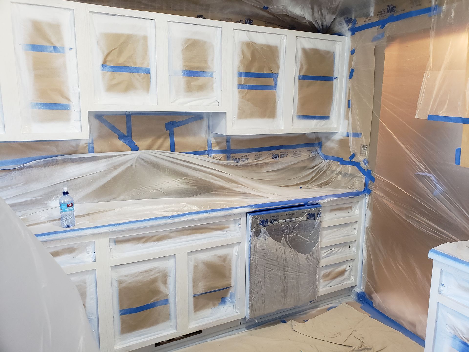 Cabinets freshly sprayed white during refinishing, with masking still in place before reassembly