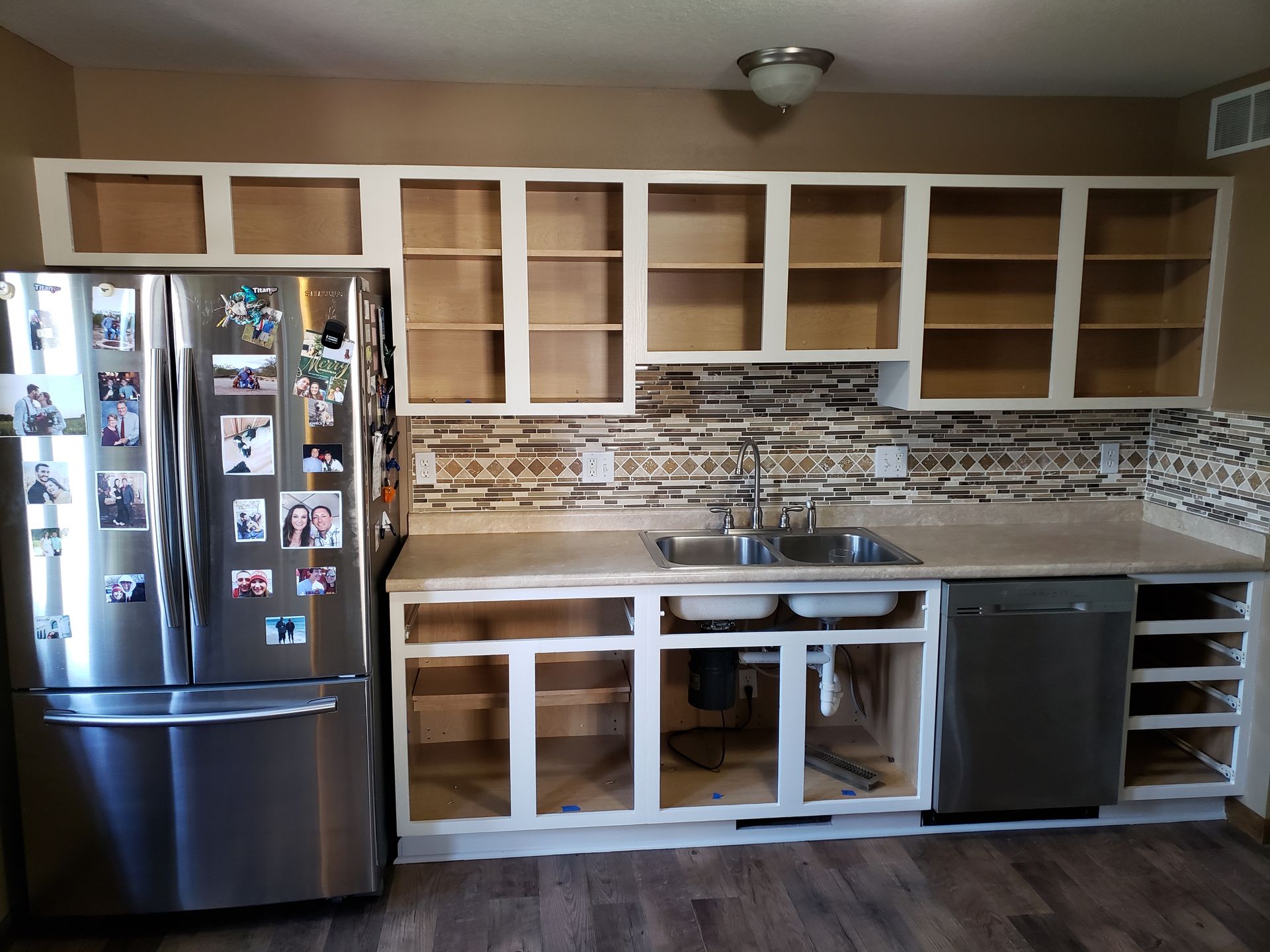 Cabinet refinishing in progress with white-painted frames and doors removed, showing shelves and plumbing