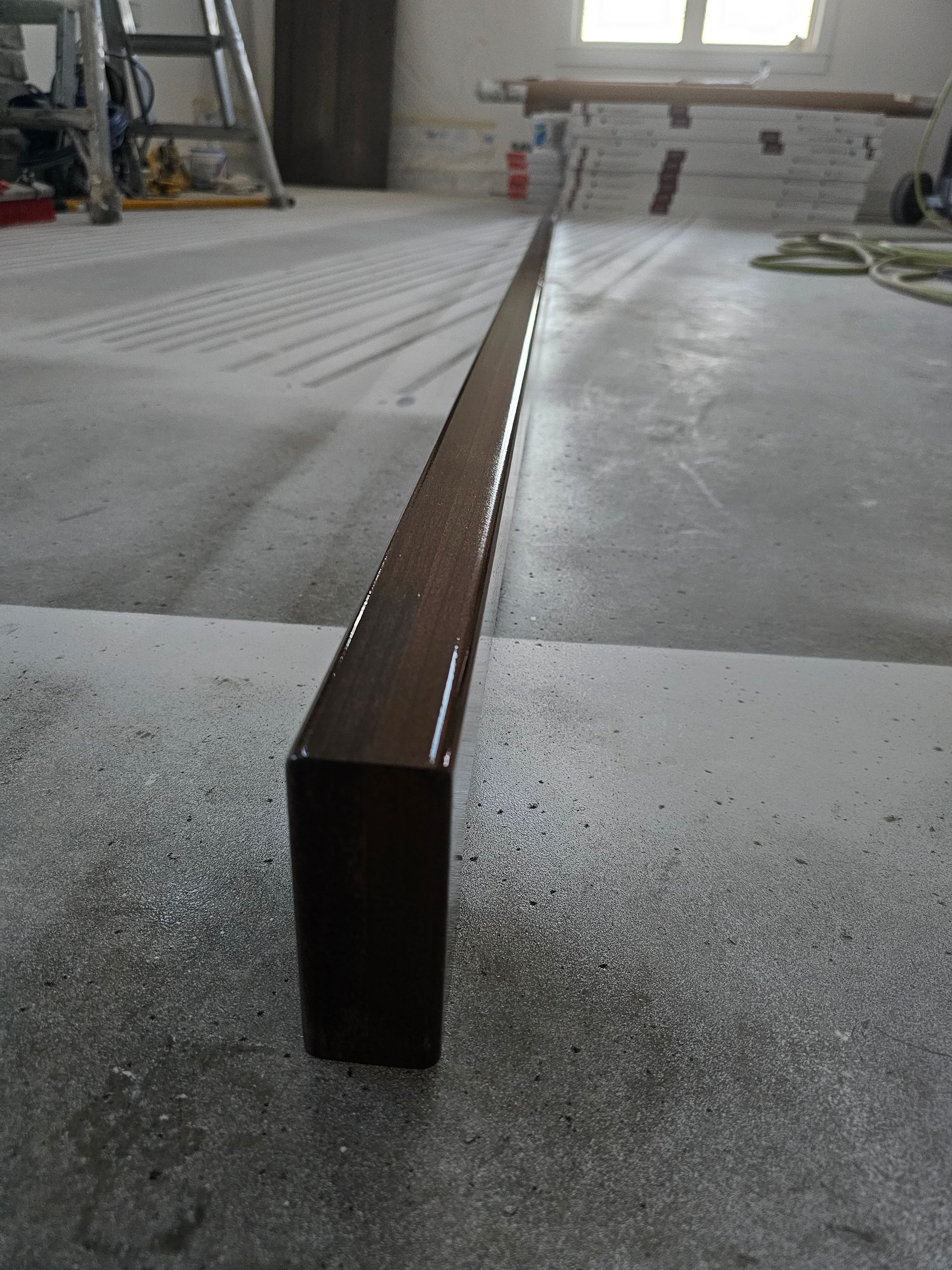 Close-up of freshly stained wood handrail on concrete floor with smooth, glossy finish