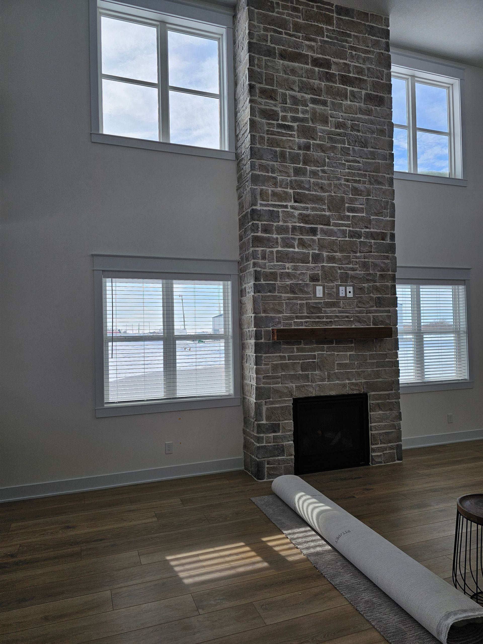 Living room with vinyl plank flooring, tall stone fireplace, and large white-trimmed windows