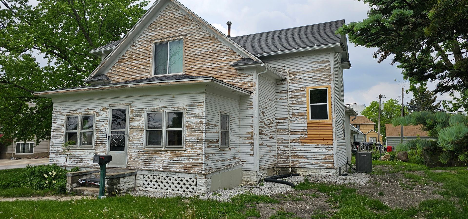 Old two-story home with peeling white paint and exposed wood siding before exterior restoration