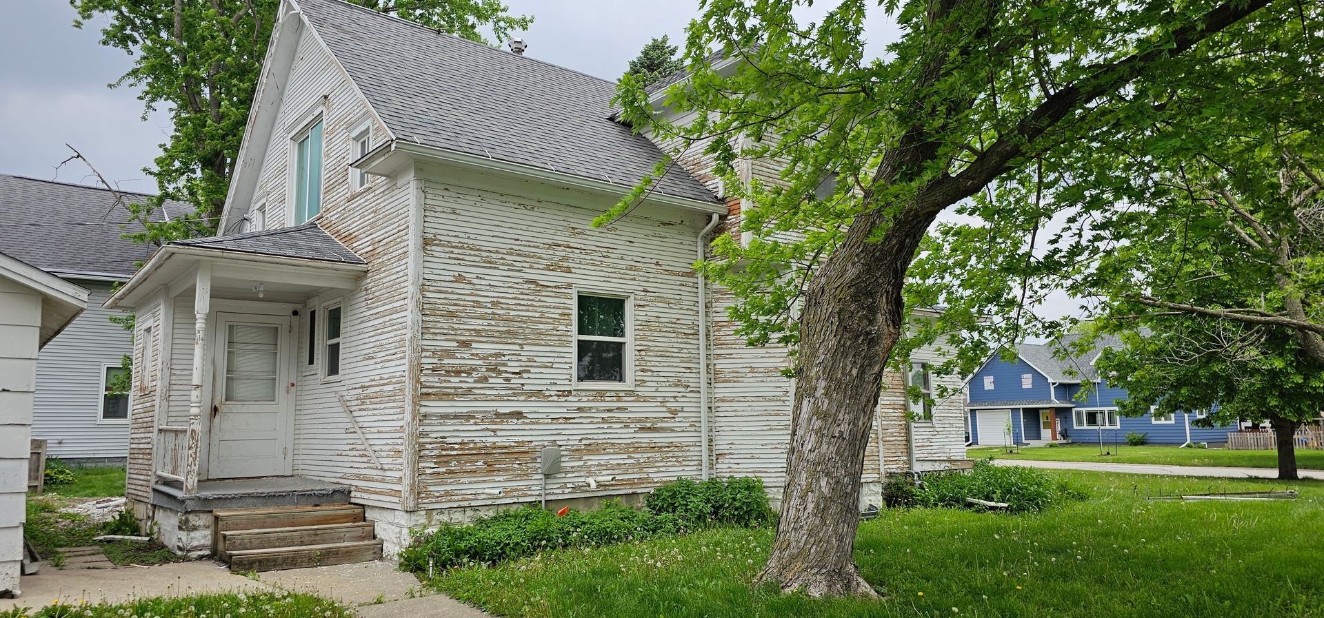Weathered two-story house with peeling white paint and exposed wood, showing need for repainting