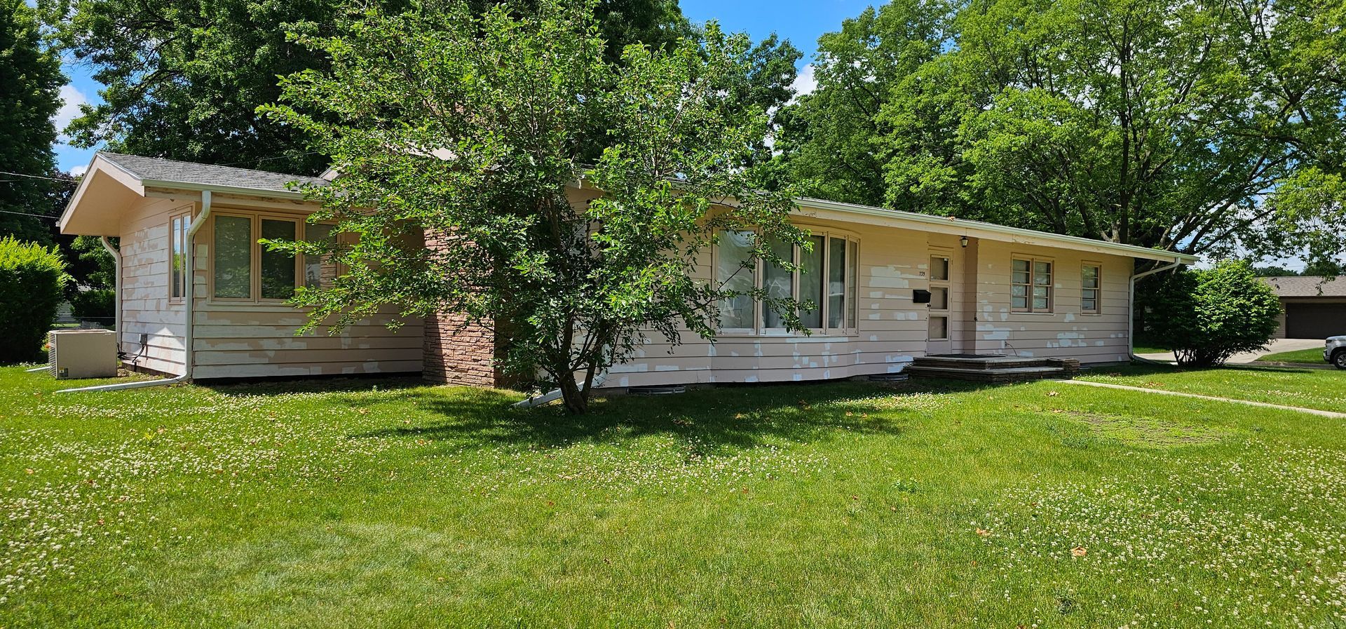 Single-story pink house prepped for exterior painting with primer spots and patchy siding