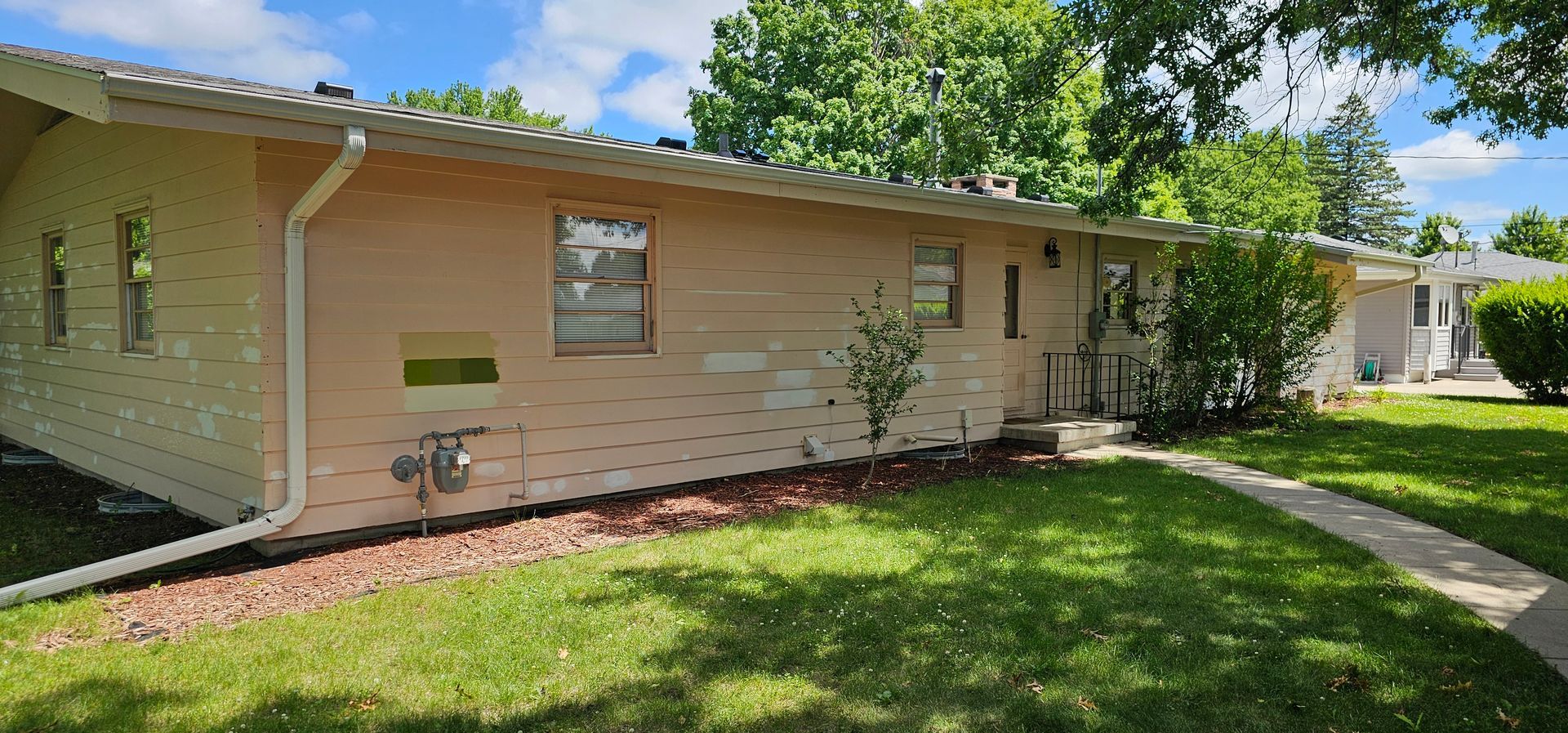 Side view of a house showing test color swatches and primed siding during the early stages of an exterior repainting project.