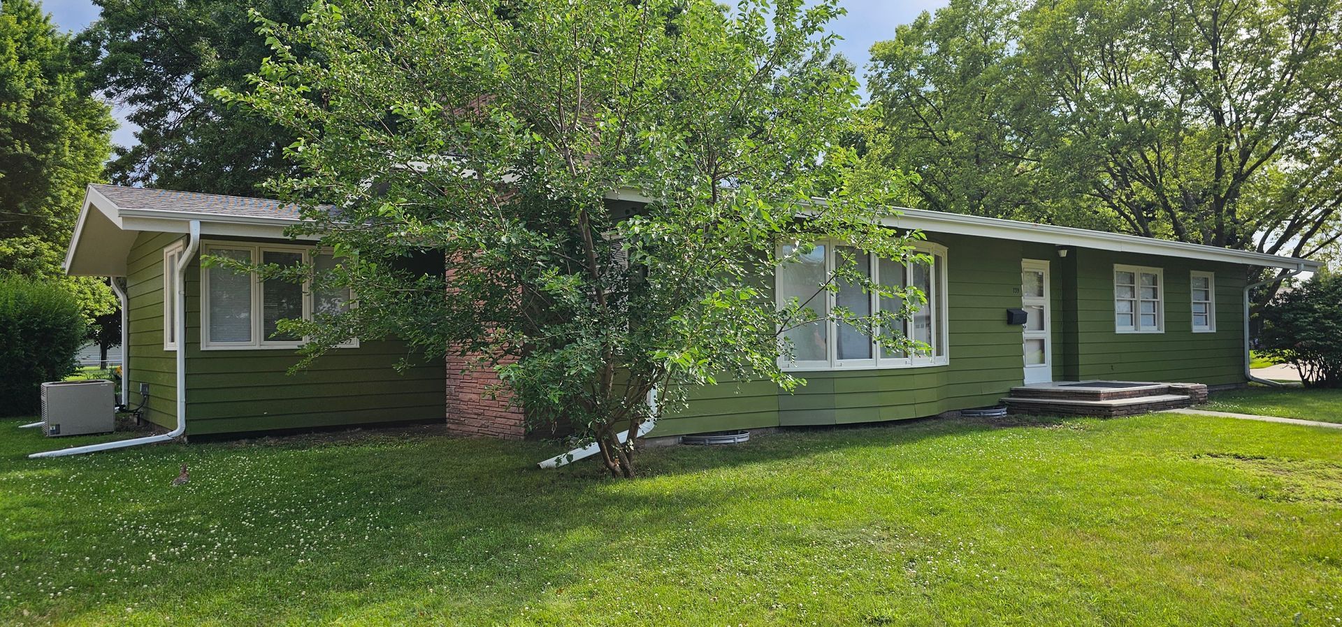 Angled front view of a professionally painted green ranch-style home with fresh white trim and a clean lawn.
