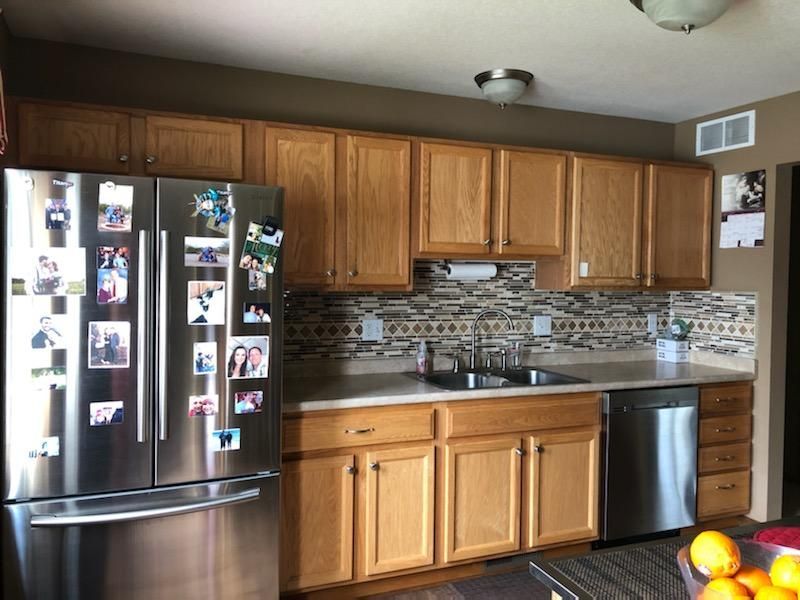 Before photo of a kitchen with natural oak cabinets, beige tile backsplash, and stainless steel appliances.