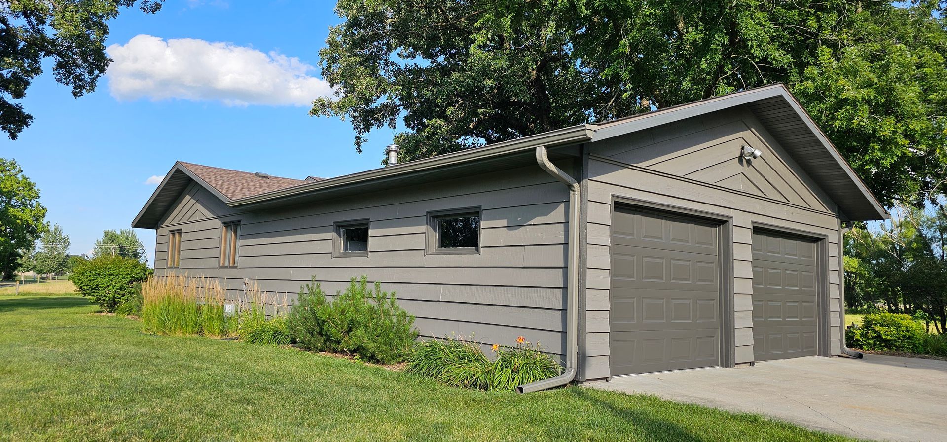 Freshly painted rural garage with brown siding, dark trim, and double doors surrounded by greenery