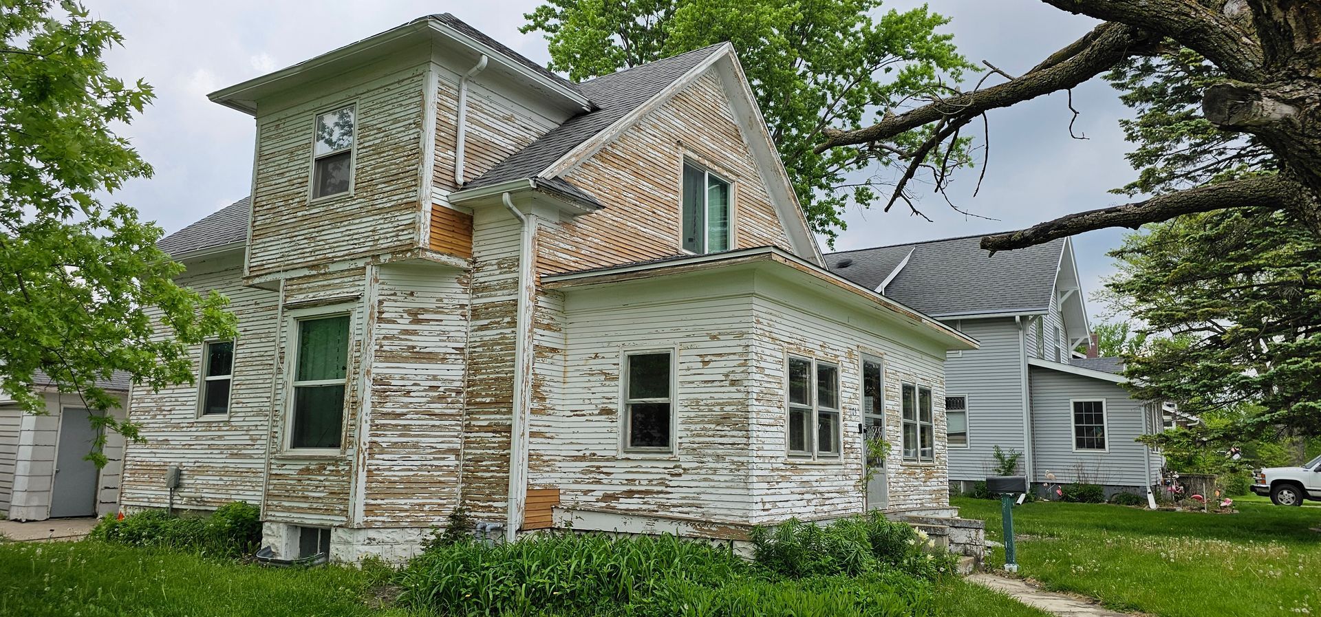 Old two-story house with peeling paint and exposed wood during prep for full exterior repaint