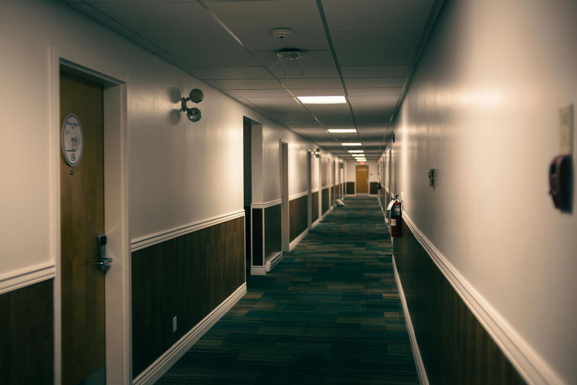 Long interior hallway of a commercial building with wood panel wainscoting, white upper walls, and blue patterned carpet