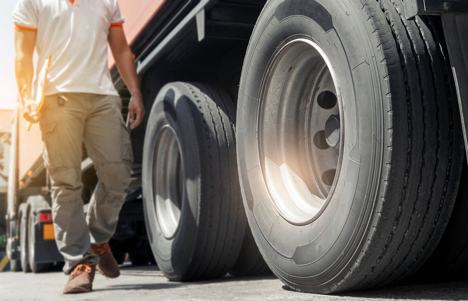 Truck driver walking near semi-truck tires. Sunlight.