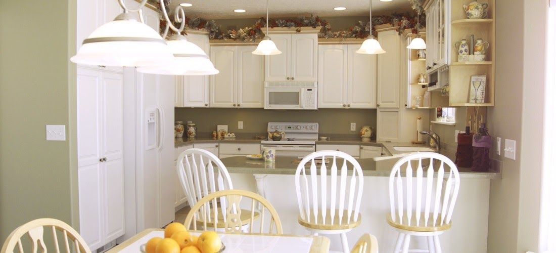 A kitchen with white cabinets and chairs and a table with a bowl of oranges on it.