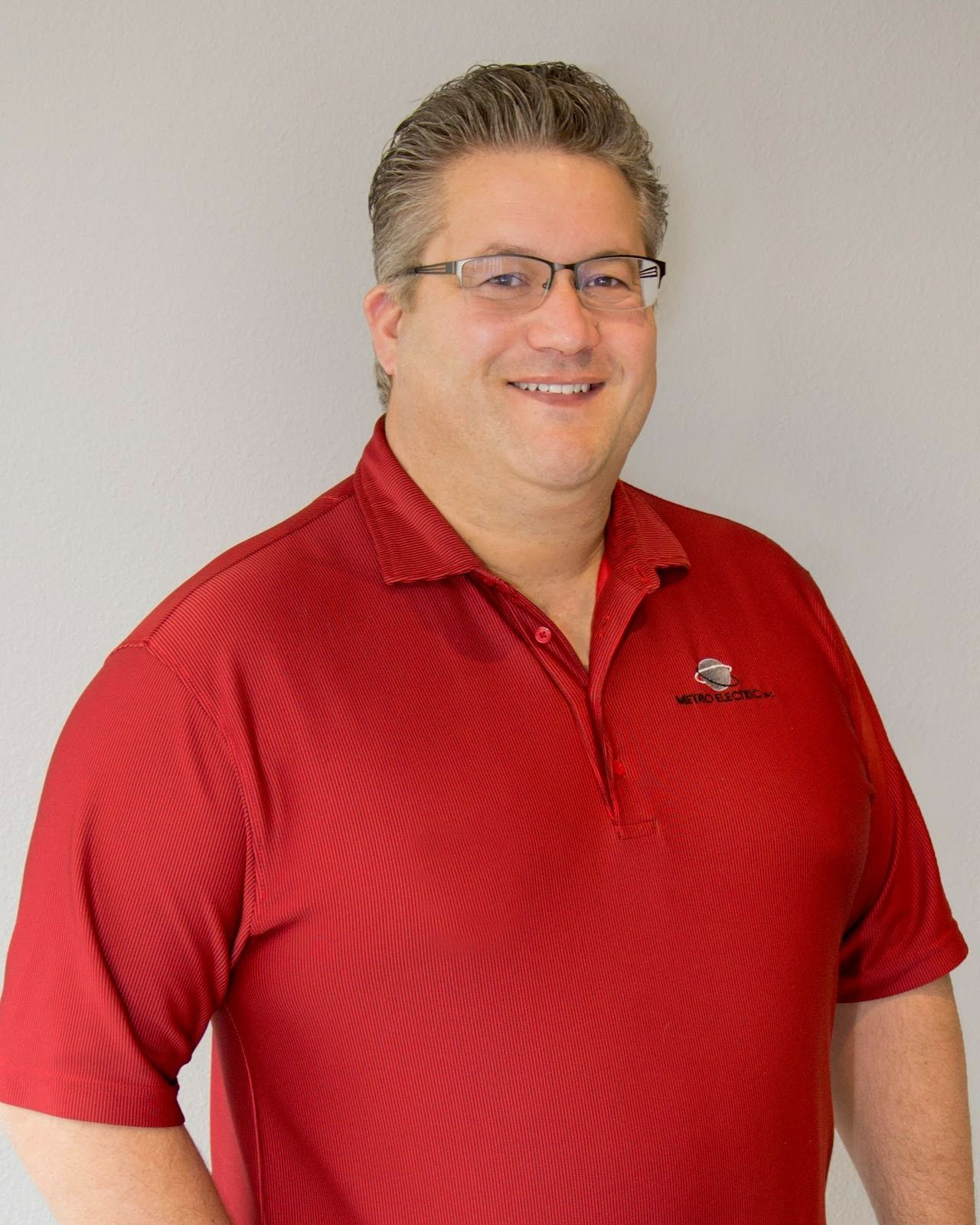 A man wearing glasses and a red shirt is smiling for the camera.