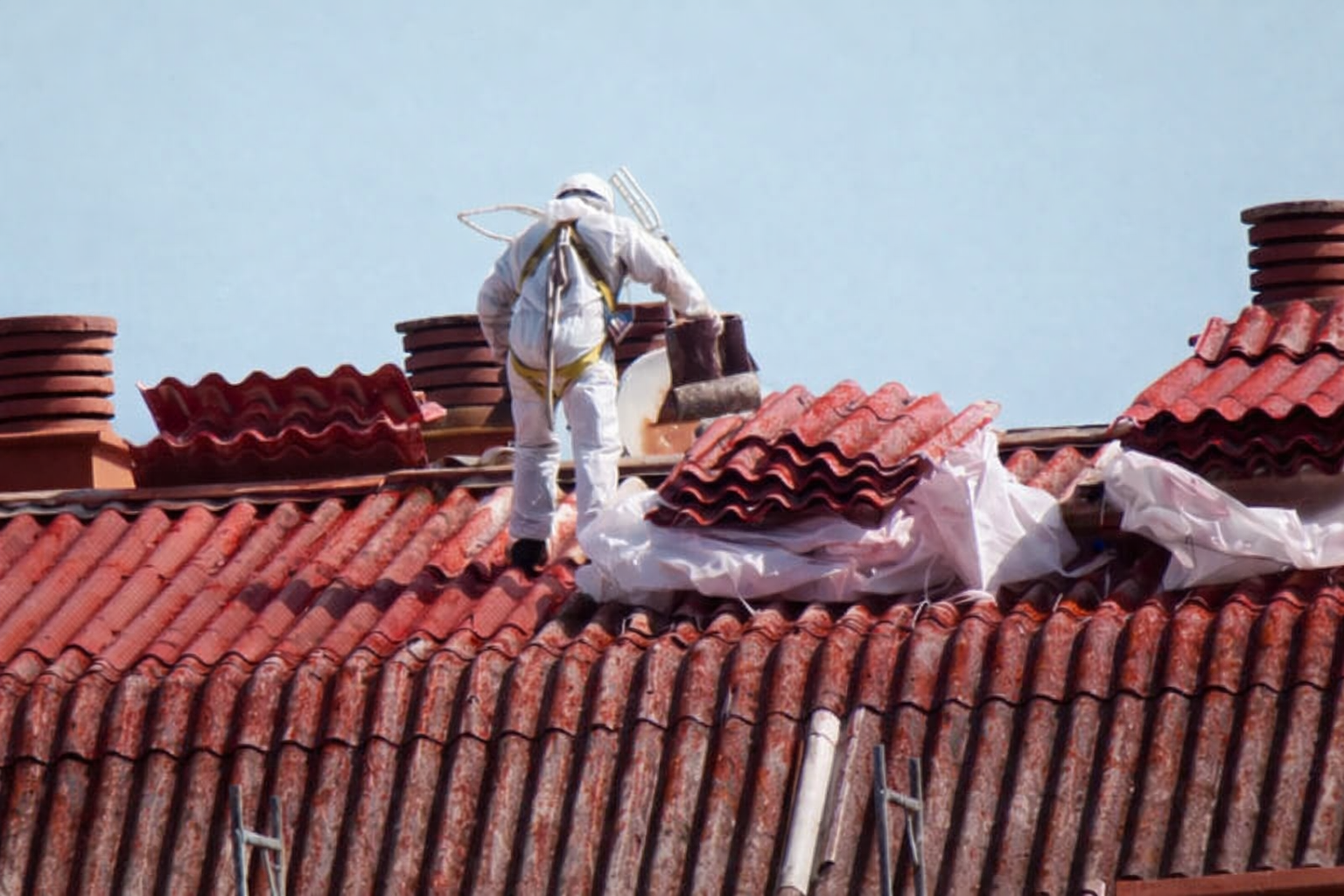 Persona in tuta protettiva che rimuove le tegole del tetto, installazione sul tetto, cielo sereno.