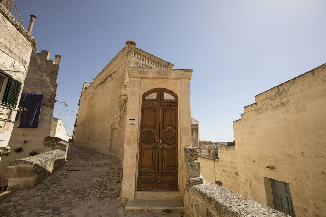 Edifici in pietra con porta in legno su una strada soleggiata.
