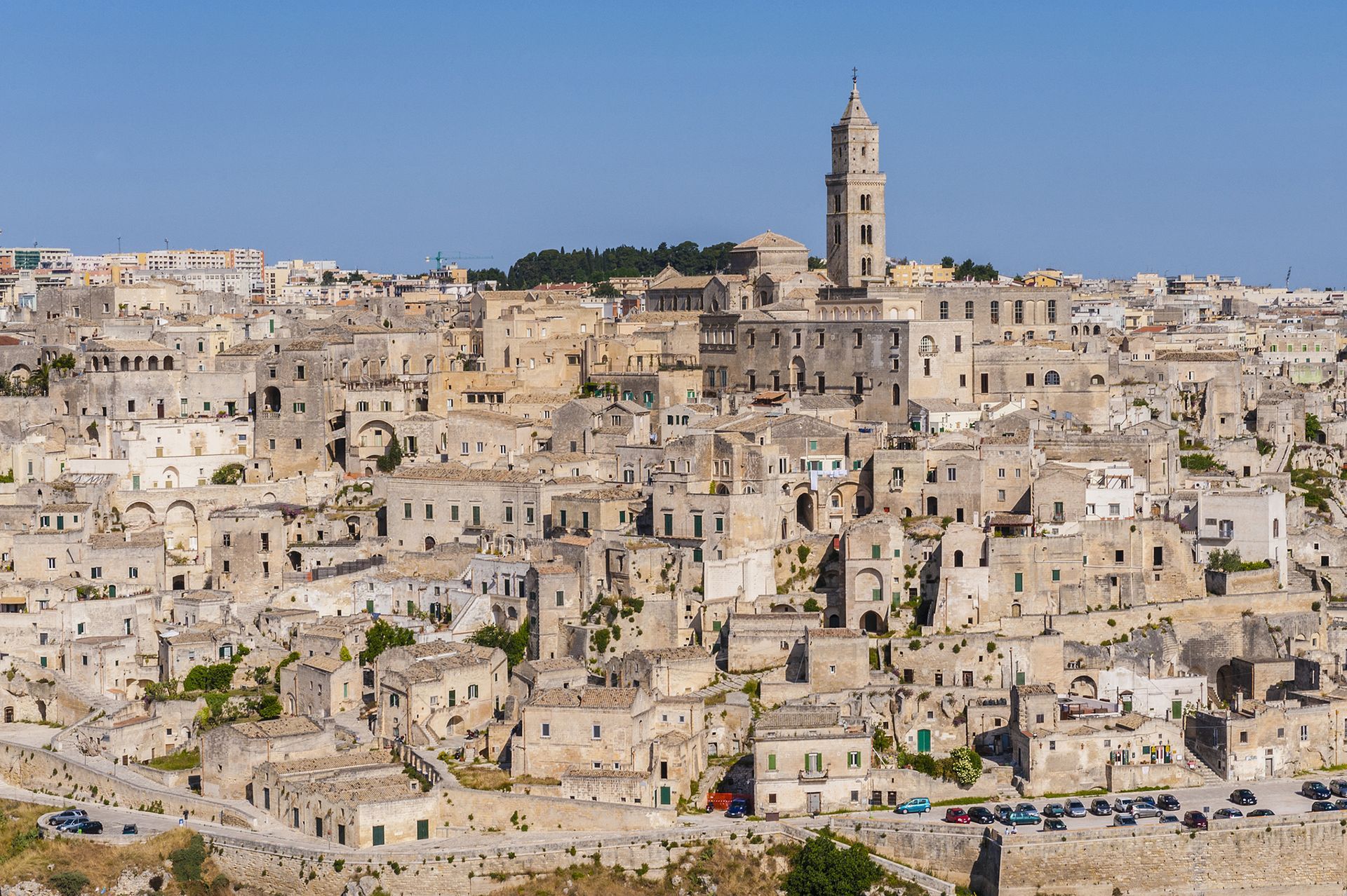 Matera, Italia, una città collinare con edifici in pietra e un alto campanile che si staglia contro un cielo azzurro.