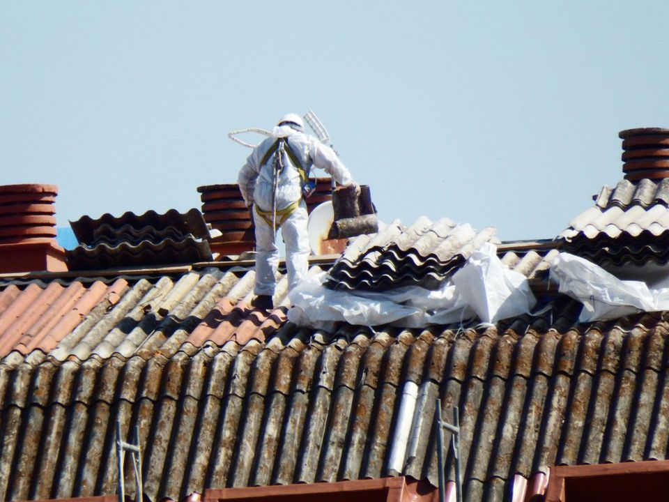 Persona in tuta protettiva che rimuove le tegole del tetto, installazione sul tetto, cielo sereno.