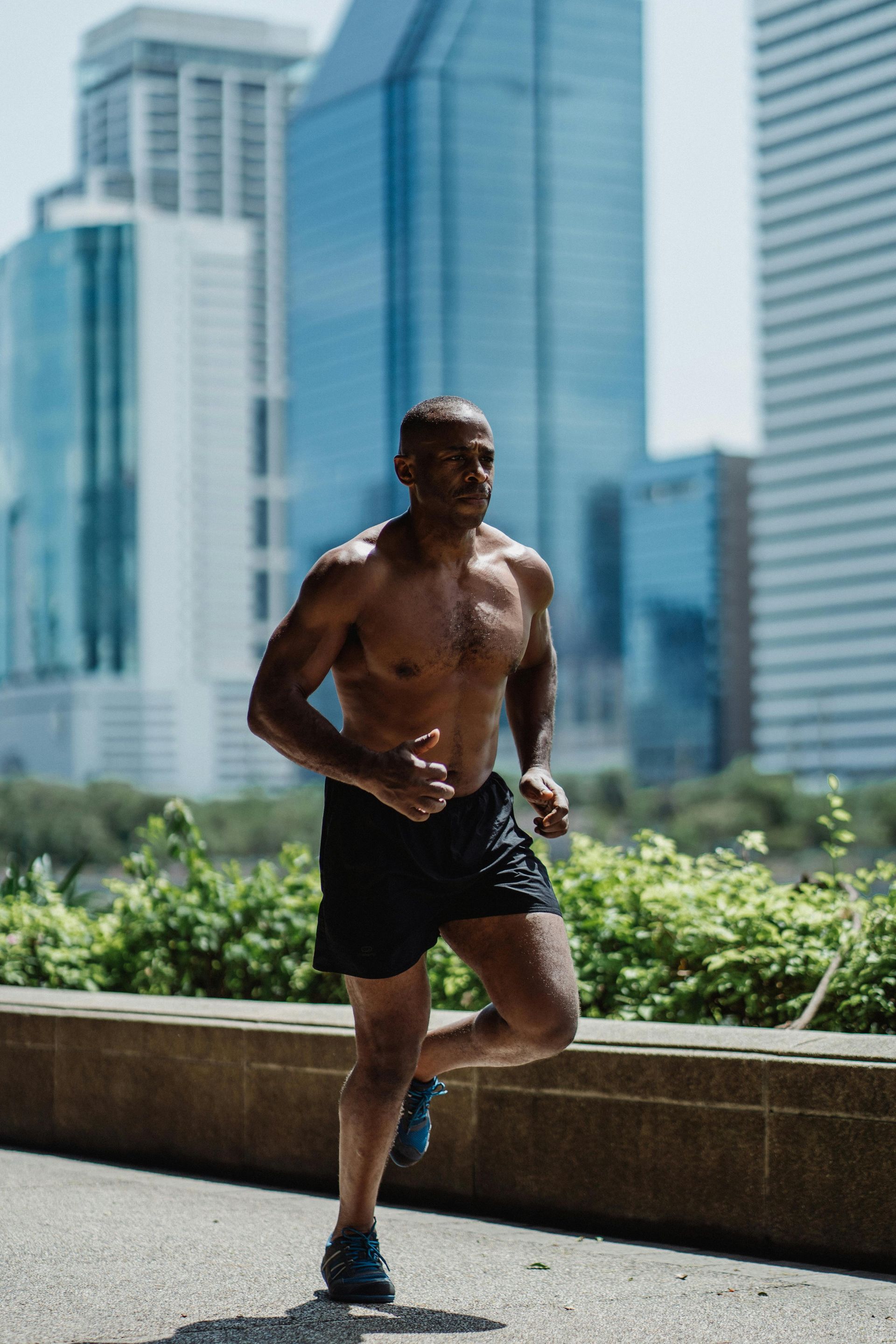 A shirtless person runs outdoors in front of city buildings.