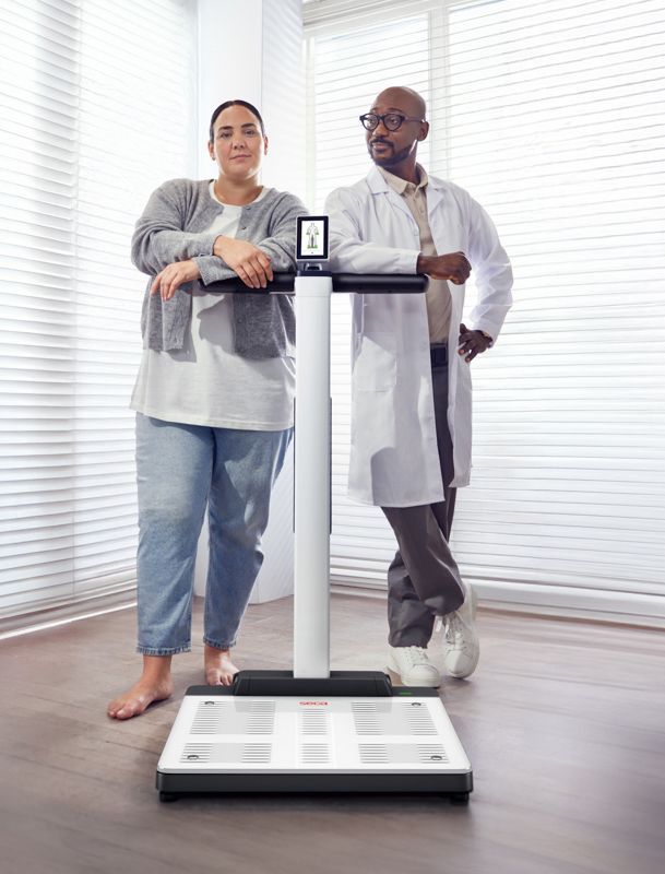 Two people standing on a body composition scale in a bright room
