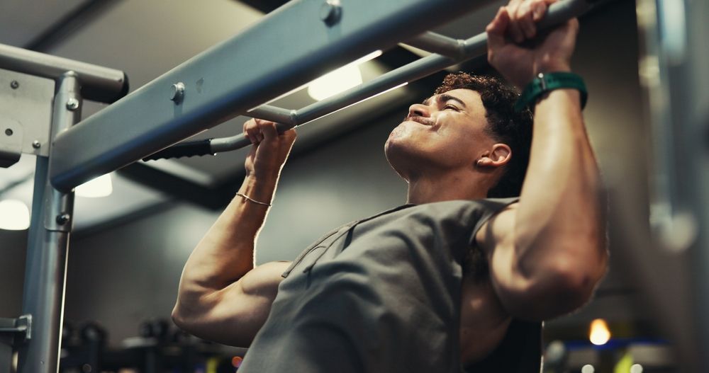 Man doing a pull-up at a gym, straining face up, gripping bar.