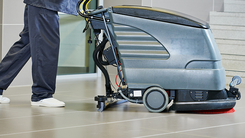 A woman in an apron is cleaning a wooden table with a towel.